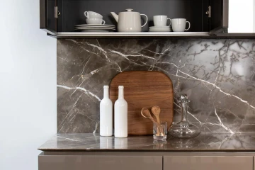 Detalle de objetos en una cocina con botellas y tazas en un armario abierto